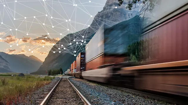 Freight train travels towards sunrise through a mountainous landscape while a digital data network is spreading out from the vehicle.