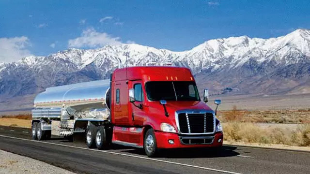 Freightliner Cascadia truck from Daimler driving through the plains in the USA with snow-capped mountains in the background.