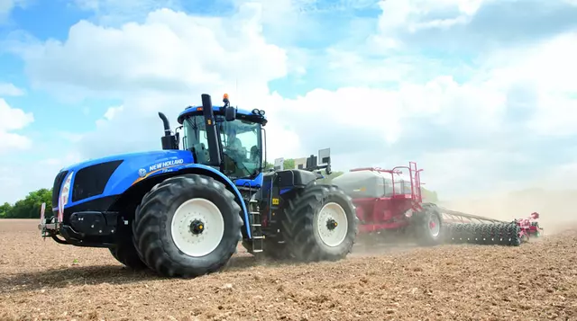 A New Holland tractor up close driving across the field with a machine in tow.